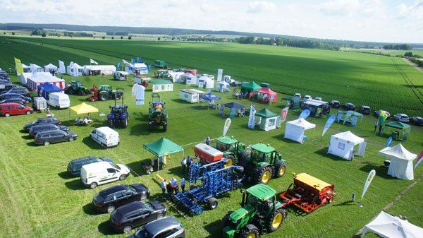 Drohnenaufnahme einer landwirtschaftlichen Messe oder Ausstellung auf einem Feld mit Traktoren, Maschinen, Zelten und Besuchern.