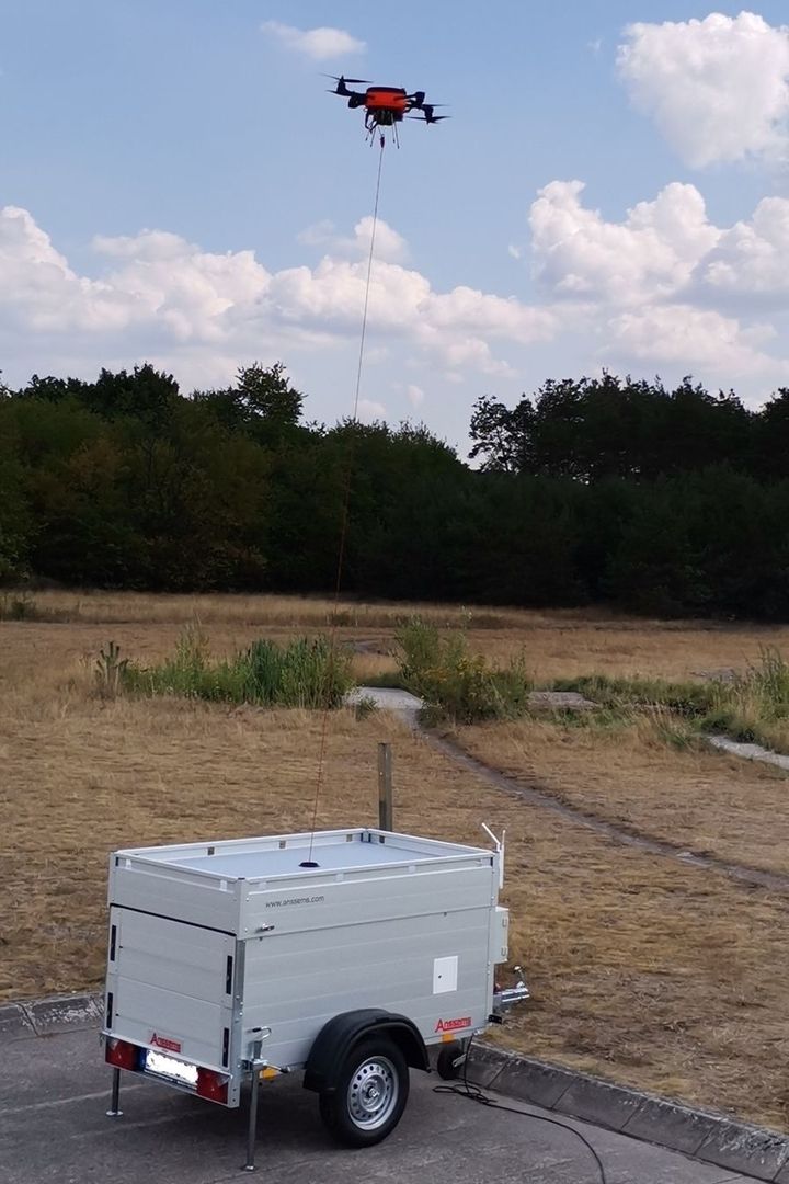 Tethered Drohne im Flug verbunden mit mobiler Bodenstation auf Anhänger in trockener Landschaft